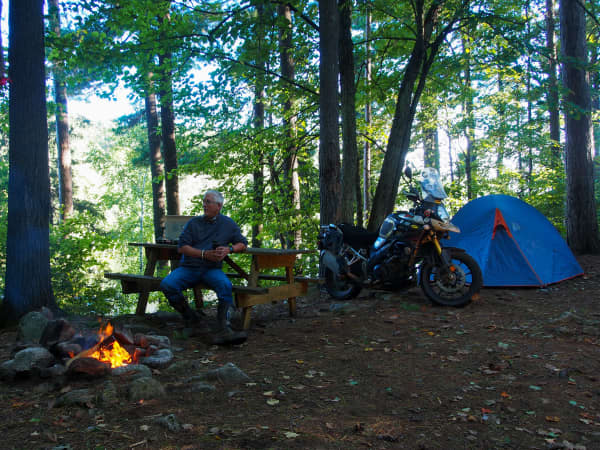 motorcyclist sitting at campfire with Suzuki VStrom and tent