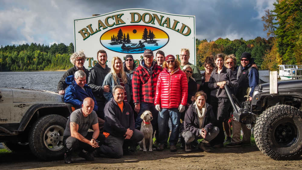 Eastern Ontario Trail Blazers group photo in front of Black Donald Tent and Trailer Park sign in front of lake