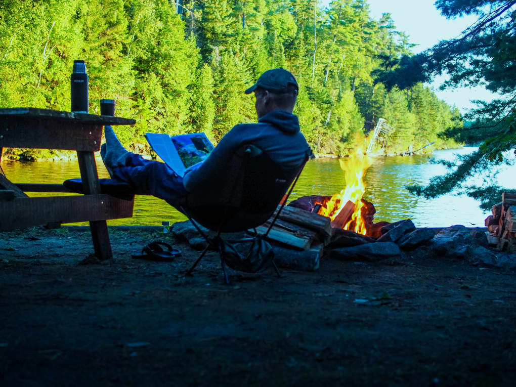 a camper relaxing by the fire and reading a magazine