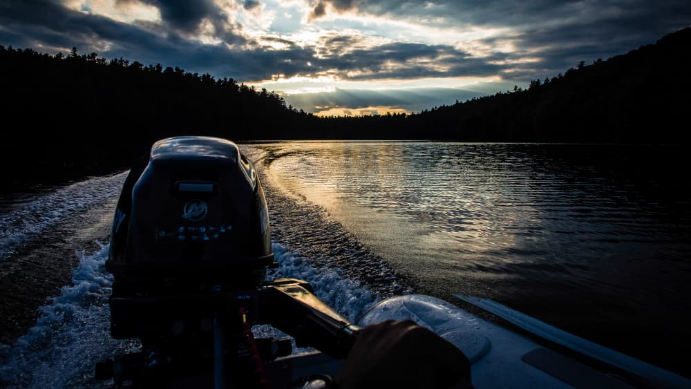 wake behind a zodiac with a 9.9 Merc outboard and the sunsetting over the water